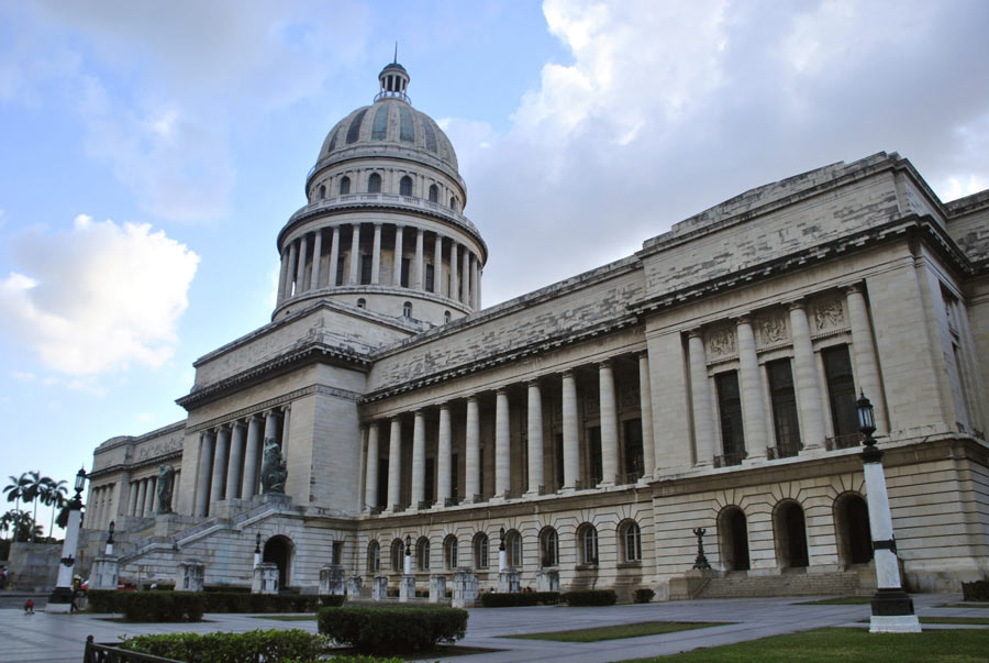 Grand domed National Capitol Building of Havana with towering columns under a partly cloudy sky, viewed from the front plaza.