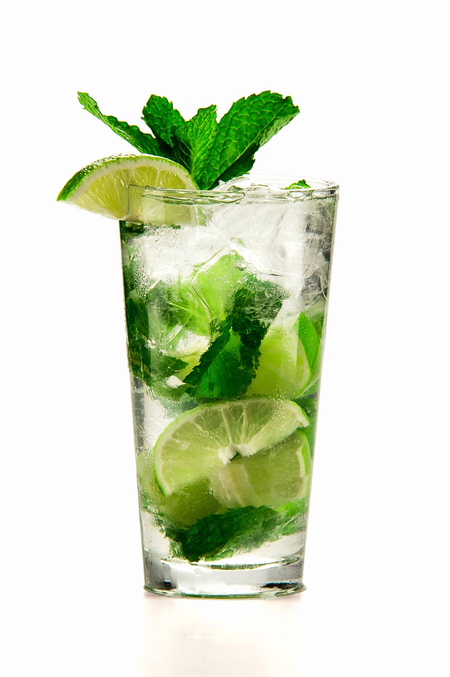 A tom collins glass of a mojito cocktail with ice, lime slices, fresh mint leaves and a lime wedge garnish against a white background.
