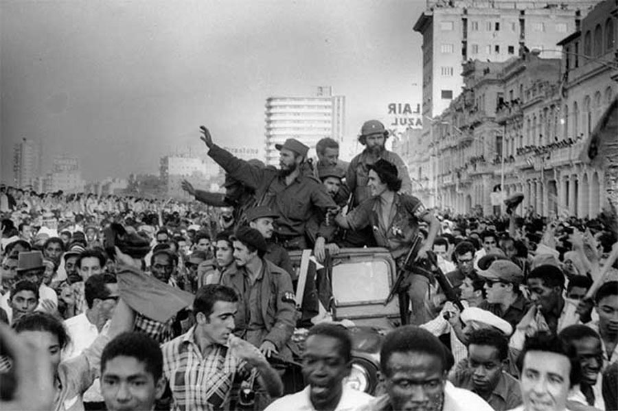 Black-and-white photo of a jubilant crowd surrounding a Jeep carrying Fidel Castro and his rebels through Habana’s streets.