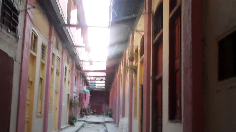 The interior hallway of a typical Havana solar housing painted in bright pink with skylights overhead and a few people gathered in the distance.